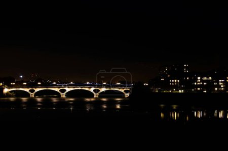 Photo for Night view of lights from the windows of the residential buildings of Bazacle Promenade Dike, in Toulouse, France, and Pont des Catalans Bridge crossing the river Garonne with reflection in the water - Royalty Free Image