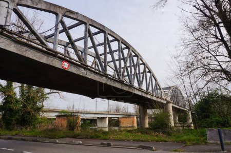 Photo for The old abandoned bow-string bridge Pont d'Empalot crossing the river Garonne in Toulouse, France, seen from the embankment ; built in 1910, now closed, it features lateral concrete lattice beams - Royalty Free Image