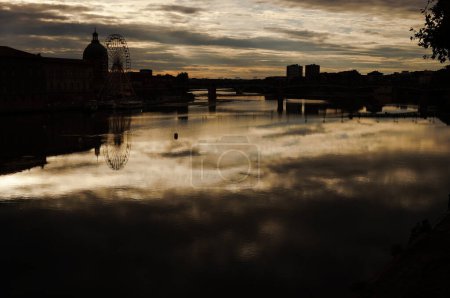 Téléchargez les photos : Skyline de Toulouse dans l'obscurité dans un coucher de soleil nuageux, avec reflet dans l'eau de la Garonne, avec la silhouette du Dôme de Lagrave, la roue la plus ferrée et le pont Saint-Pierre - en image libre de droit