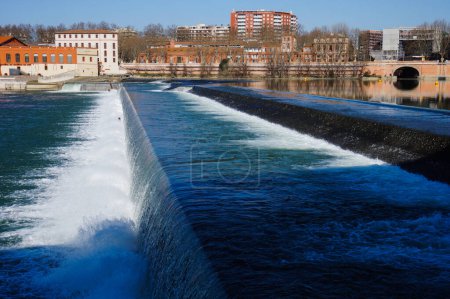 Foto de Toulouse, France - Waterfall producing white foam and whirlpool on the river Garonne, downstream the bridge Pont Saint-Pierre, seen from Viguerie Passerelle, in Saint-Cyprien district - Imagen libre de derechos