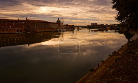 Téléchargez les photos : Coucher de soleil sur la Garonne traversant le centre historique de Toulouse, en France, en aval du pont de Saint-Pierre et de l'église dôme de La Grave, avec des reflets du ciel dans l'eau - en image libre de droit