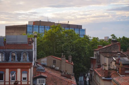 Téléchargez les photos : Toulouse, France - Juin 2021 - Un immeuble de bureaux avec une façade vitrée, et des toits de vieilles maisons traditionnelles en briques du Sud, vues à l'aube depuis le parking Victor Hugo, dans le quartier Arnaud Bernard - en image libre de droit