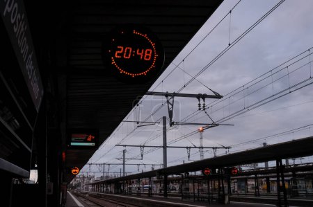 Photo for Toulouse, France - Jan. 2020 - Night shot in Toulouse-Matabiau train station, with an electronic clock telling time in 24-hour format hanged over the platforms and overheads lines above the tracks - Royalty Free Image