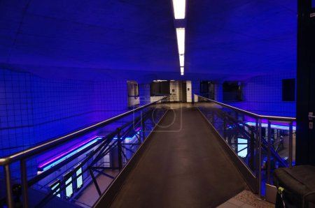 Photo for Toulouse, France - Aug. 2022 - Modern interior of the tube station of Matabiau Train Station, illuminated by night with blue and purple lights ; the pedestrian walkway that overhangs the transfer hall - Royalty Free Image