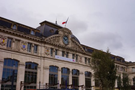 Foto de Toulouse, Francia - Nov. 2019 - Fachada principal monumental de la Gare de Toulouse-Matabiau, la estación central de tren de la ciudad de Rose, con un gran reloj, grandes ventanales y bandera francesa - Imagen libre de derechos