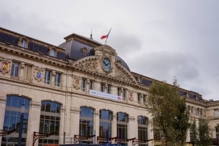 Foto de Toulouse, Francia - Nov. 2019 - Fachada principal monumental de la Gare de Toulouse-Matabiau, la estación central de tren de la ciudad de Rose, con un gran reloj, grandes ventanales y bandera francesa - Imagen libre de derechos