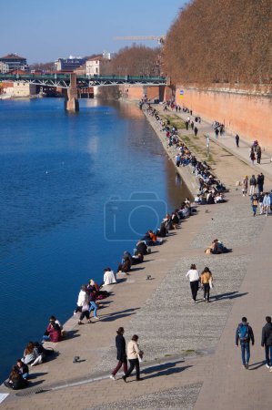 Téléchargez les photos : Toulouse, France - Mars 2023 - Rive de la Garonne, en contrebas de la Promenade Henri Martin, entre les places Saint-Pierre et Daurade ; les gens se refroidissent au bord de l'eau bleue, d'autres flânent sur la promenade - en image libre de droit