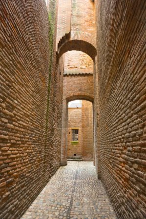 Efecto perspectivo en una calle típica estrecha con paredes de ladrillo, pavimento y puertas de arco dentro del complejo arquitectónico medieval del Convento de Jacobinos, en Toulouse, la ciudad de Rose, Francia