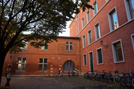 Foto de Toulouse, Francia - Nov. 2019 - Edificio de ladrillo del Liceo Pierre de Fermat, que incluye una parte más antigua del castillo de Bernuy con ventanas de muntin renacentistas y puerta abovedada; estacionamiento de bicicletas en el patio - Imagen libre de derechos