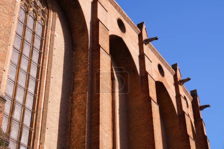 Foto de Cara sur de la iglesia construida en ladrillo del Convento Jacobino, en Toulouse, Francia, un monumento medieval gótico-meridional, con grandes vidrieras, imponentes contrafuertes y gárgolas a lo largo del techo - Imagen libre de derechos