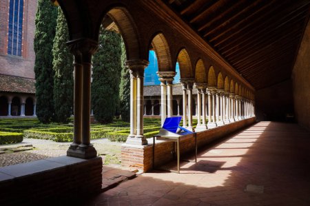 Photo for Toulouse, France - April 2019 - Cloister and French garden with cypress tree and trimmed bushes, in the Dominican Convent ofJacobins, a medieval brick monastery housing Thomas Aquinas' burial - Royalty Free Image