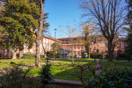 Foto de Toulouse, Francia - Feb. 2019 - El bucólico y frondoso jardín Aym Kung en la plaza de Bolonia, bordeado por el edificio de ladrillo del Conservatorio Regional de Música, y detrás, el Liceo Pierre de Fermat - Imagen libre de derechos