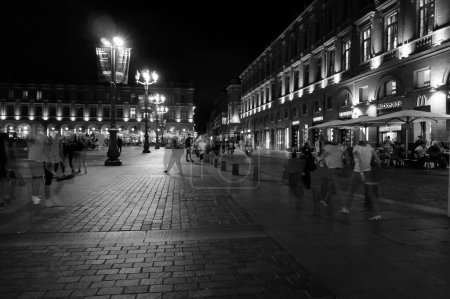 Foto de Toulouse, Francia - Dic. 2018- La vida nocturna en un lugar popular de la ciudad rosa, con gente pasando el rato en la plaza del Capitolio pavimentada, terrazas de restaurantes con sombrillas, tiendas y edificios iluminados - Imagen libre de derechos