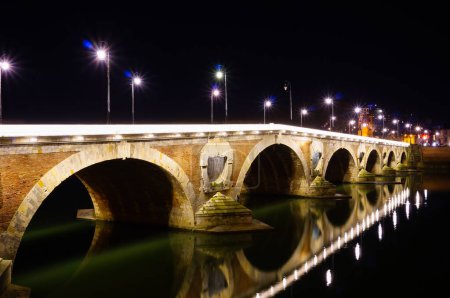 Téléchargez les photos : Plan nocturne du pont voûté en brique Pont-Neuf, le plus ancien pont de Toulouse, France, avec des ouvertures (voûtes de sortie) pour résister aux inondations, et réflexion de la lumière dans l'eau de la Garonne - en image libre de droit