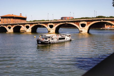 Foto de Toulouse, Francia - Julio 2020 - Una barcaza de cruceros que embarca a los turistas en la cubierta para un recorrido turístico por el río Garona, navega río abajo el puente de arco de ladrillo de Pont-Neuf, cerca del Htel-Dieu - Imagen libre de derechos