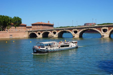 Foto de Toulouse, Francia - Julio 2020 - Una barcaza de cruceros que embarca a los turistas en la cubierta para un recorrido turístico por el río Garona, navega río abajo el puente de arco de ladrillo de Pont-Neuf, cerca del Htel-Dieu - Imagen libre de derechos