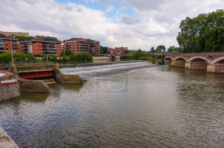 Photo for Massive metal valve of a sluice-gate in Tounis neighborhood, put in motion by hydraulic cylinders, in Toulouse, France, with the River Garonne flowing under the bridge of Saint-Michel in the back - Royalty Free Image