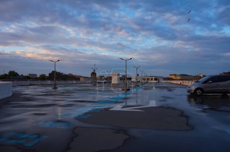 Téléchargez les photos : Toulouse, France - Juin 2021 - Puddles sur l'asphalte humide du dernier niveau du parking Victor Hugo dans le quartier Arnaud Bernard, à l'aube, avec des reflets du ciel rose et jaune dans l'eau - en image libre de droit