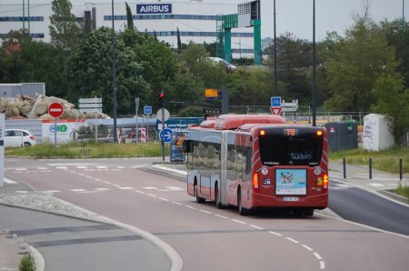 Foto de Toulouse, Francia - 10 de junio de 2023 - Un autobús urbano articulado y rojo operado por la empresa de transporte Tisso conduce por Montaudran Innovation Campus, hacia la fábrica Airbus Defence and Space en Labge - Imagen libre de derechos