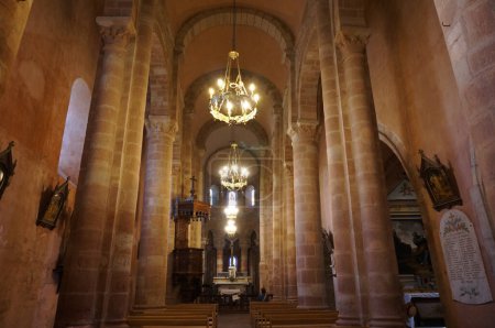 Téléchargez les photos : Bozouls, France - 14 août 2023 - Nef à l'intérieur du XIIe siècle, église médiévale Sainte-Fauste ; lustres suspendus au plafond, dont les voûtes en berceau romanes sont soutenues par des piliers de pierre - en image libre de droit