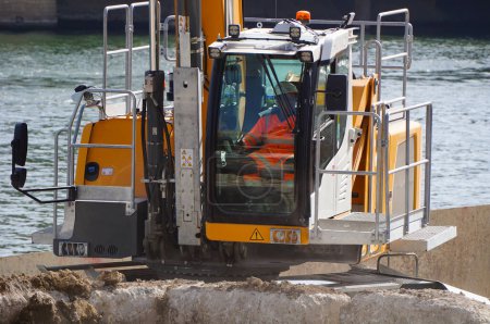 Foto de París, Francia - 6 de septiembre de 2023 - Cabina del operador una excavadora Liebherr amarilla en acción en un muelle, junto al agua, en Port de Tolbiac, un puerto industrial en el río Sena, en el distrito 13 - Imagen libre de derechos