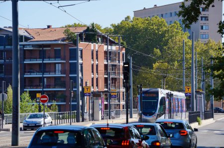 Foto de Toulouse, Francia - 7 de octubre de 2023 - Paisaje urbano al final del puente Saint-Michel: el tráfico de automóviles con vehículos se detiene en un semáforo rojo, un tranvía en la línea Tisso T1 sale de la estación Ile du Ramier - Imagen libre de derechos