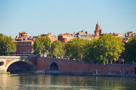 Foto de Toulouse, Francia - 7 de octubre de 2023 - Lente larga, vista de verano sobre el ladrillo, puente arqueado de Pont-Neuf, con cruces del río Garona, sobre la Basílica de Daurade y el Convento de Jacobinos, un hito medieval - Imagen libre de derechos
