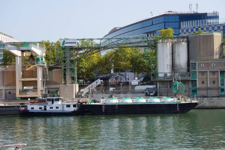 Téléchargez les photos : Paris, France - 5 septembre 2023 - Un méthanier fluvial, avec réservoirs sphériques, navigue sur la Seine, passant devant une cimenterie Lafarge dans le port de Tolbiac, dans le 13ème arrondissement - en image libre de droit