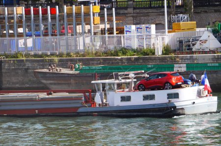 Foto de París, Francia - 5 de septiembre de 2023 - Un barco de fondo plano francés navega por el río Sena en Tolbiac Port, en el distrito 13, transportando un coche compacto Renault Clio rojo en la plataforma en la parte posterior - Imagen libre de derechos