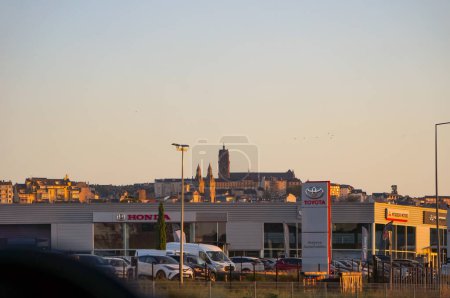 Photo for Rodez, France - Aug. 14, 2023 - Sunset view in Rodez, chief-city of Aveyron: in the forefront, Japanese car dealerships; in the background, the old quarters up the hill and Notre Dame cathedral - Royalty Free Image
