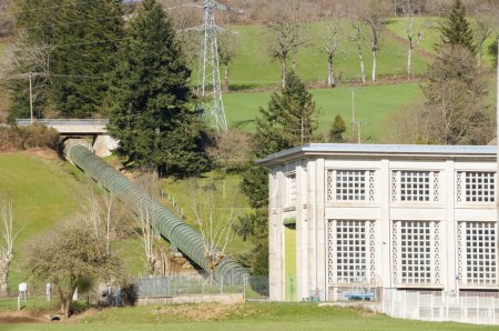 Téléchargez les photos : Villefranche-de-Panat, France - 2 avril 2023 - Centrale hydroélectrique au bord du lac de Panat : une conduite d'eau conduit l'eau de l'amont aux turbines, alors qu'elle tombe du versant montagneux - en image libre de droit