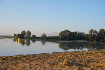 Téléchargez les photos : Graudot, France - 9 septembre 2023 - Plage sauvage au coucher du soleil au bord du lac de la Forêt d'Orient, près de Troyes (Aube), regardant vers le promontoire de la Petite Italie ; le sol est couvert de mousses aquatiques - en image libre de droit