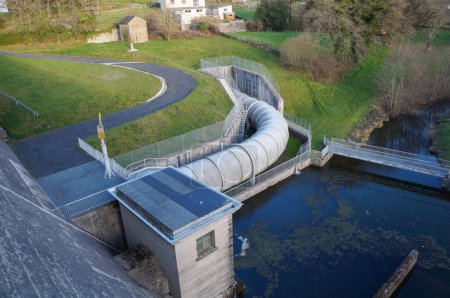 Foto de Villefranche-de-Panat, Francia - 2 de abril de 2023 - Estructuras de ingeniería civil al pie de la presa del lago del pueblo de Panat, junto a la central hidroeléctrica, con tuberías y piscinas para la descarga de agua - Imagen libre de derechos
