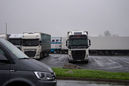 Foto de Limousin, Francia - 26 de diciembre de 2022 - Un semirremolque DAF blanco llega a un estacionamiento y maniobra entre otros camiones para conseguir un lugar, en una zona de descanso junto a la autopista, en un día de invierno lluvioso y frío. - Imagen libre de derechos