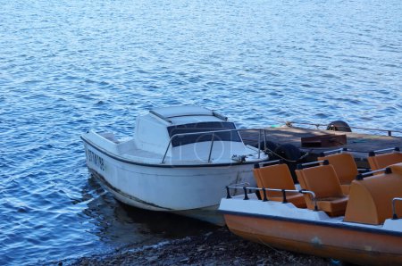 Téléchargez les photos : Villefranche-de-Panat, France - 6 avril 2023 - Un petit bateau blanc avec un cockpit couvert amarré à une jetée sur le lac Villefranche-de-Panat, un lac de montagne dans la zone rurale de Lvzou, en Aveyron - en image libre de droit