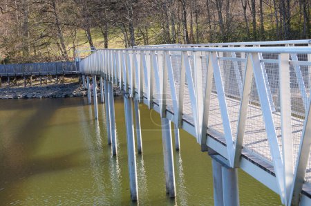 Foto de Villefranche-de-Panat, Francia - 6 de abril de 2023 - Moderna pasarela de acero construida sobre el agua, para permitir a los peatones cruzar de una orilla del lago Panat a otra, en el Aveyron agrícola - Imagen libre de derechos