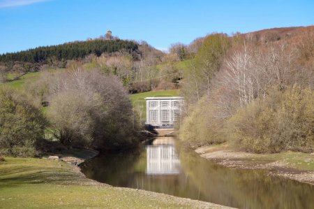 Foto de Villefranche-de-Panat, Francia - 2 de abril de 2023 - Calma la producción de agua corriente abajo de una central hidroeléctrica situada en la orilla del lago Panat, cuyo edificio se refleja en el agua, en el Aveyron rural - Imagen libre de derechos