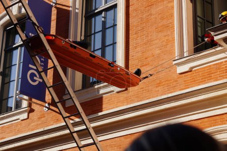 Foto de Toulouse, Francia - 7 de octubre de 2023 - Demostración en vivo del equipo de Búsqueda y Rescate en el Congreso Nacional de Bomberos: una víctima en una camilla es evacuada a través de una ventana con una escalera - Imagen libre de derechos