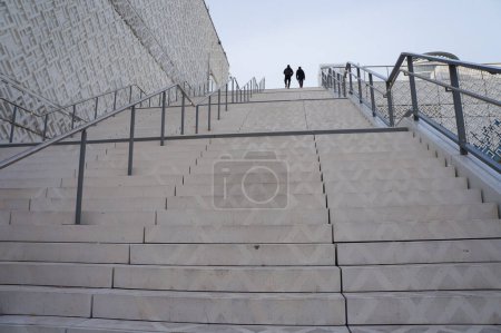 Photo for Lyon, France - Nov. 21, 2022 - Afar, silhouette of two men arriving at the top after going up a monumental outdoor staircase outside Westfield Shopping Center, in La Part-Dieu Financial District - Royalty Free Image