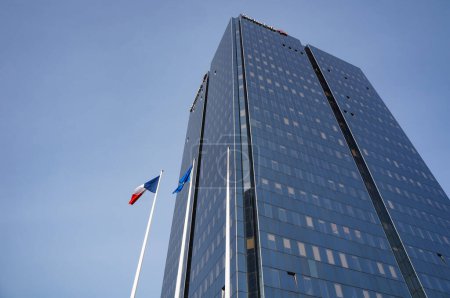 Foto de Lyon, Francia - 21 de noviembre de 2022 - Vista de bajo ángulo de la Torre de la Vida Suiza, en el distrito financiero de La Part-Dieu; banderas de Francia y la Unión Europea se ondean en sus mástiles al pie del rascacielos - Imagen libre de derechos