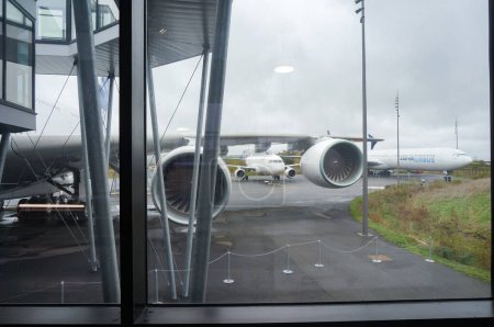 Foto de Toulouse, Francia - 21 de noviembre de 2023 - Motores bajo el ala de un jumbo jet Airbus A380 de cuerpo ancho, visto desde el cristal de la ventana de un puente de cristal que conecta la puerta de embarque con el avión - Imagen libre de derechos