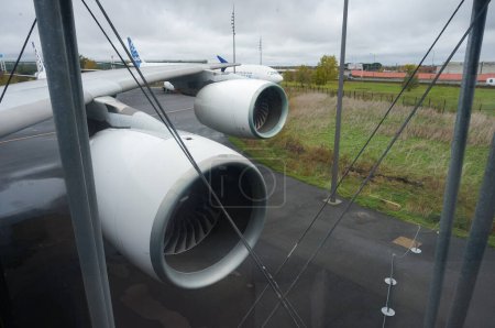 Foto de Toulouse, Francia - 21 de noviembre de 2023 - Motores bajo el ala de un jumbo jet Airbus A380 de cuerpo ancho, visto desde el cristal de la ventana de un puente de cristal que conecta la puerta de embarque con el avión - Imagen libre de derechos
