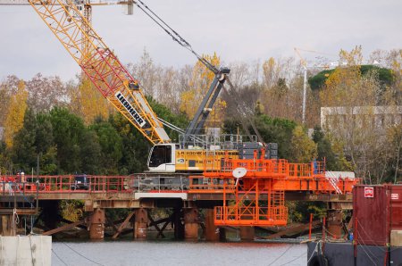 Photo for Labge, France - Dec. 2, 2023 - Crawler crane on an off-shore platform above the water, in Labge INPT Lake, on the construction site of the viaduct for the extension of the Line B of Toulouse's metro - Royalty Free Image