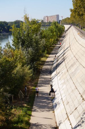 Foto de Toulouse, Francia - 7 de octubre de 2023 - Pasarela arbolada junto al río Garona, al pie del dique antiinundaciones de hormigón, en el distrito de Saint-Michel; los lugareños aprecian esta zona verde para hacer deporte - Imagen libre de derechos