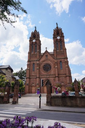 Téléchargez les photos : Espalion, France - 9 août 2023 - Saint Jean Baptiste, une église néo-gothique du XIXe siècle construite en grès rouge, avec deux clochers de 45 mètres surmontés de statues en bronze - en image libre de droit