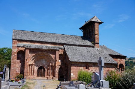 Foto de Espalion, Francia - 9 de agosto de 2023 - Cementerio del pueblo y fachada de la iglesia medieval de Saint-Hilarian-et-Sainte-Foy de Perse, construida a partir del siglo XI en piedra arenisca roja como parte de una prioridad - Imagen libre de derechos