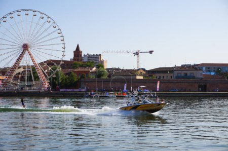 Photo for Toulouse, France - Aug. 9, 2023 - In the forefront, waterskiing on the Garonne River; in the background, the ferris wheel on Viguerie Port, Saint-Nicolas' Church in the historic Saint-Cyprien district - Royalty Free Image