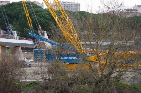 Téléchargez les photos : Toulouse, France - 23 février 2024 - Grue à anneau massive actionnée par des Sarens belges, avec un boom ici en position repliée, sur le chantier du pont suspendu Passerelle Rapas, sur l'île Ramier - en image libre de droit