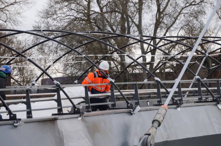 Photo for Toulouse, France - Feb. 23, 2024 - A labourer, wearing an orange reflective vest and a helmet, works on a steel cable-stayed deck, on the construction site of Passerelle Rapas, a future footbridge - Royalty Free Image