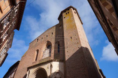 Photo for Gaillac, France - Feb. 1, 2024 - Low-angle view of the front of Saint-Pierre's, a 12th century Southern Gothic church; it features a brick tower, a stone portal and an arched window in the facade - Royalty Free Image